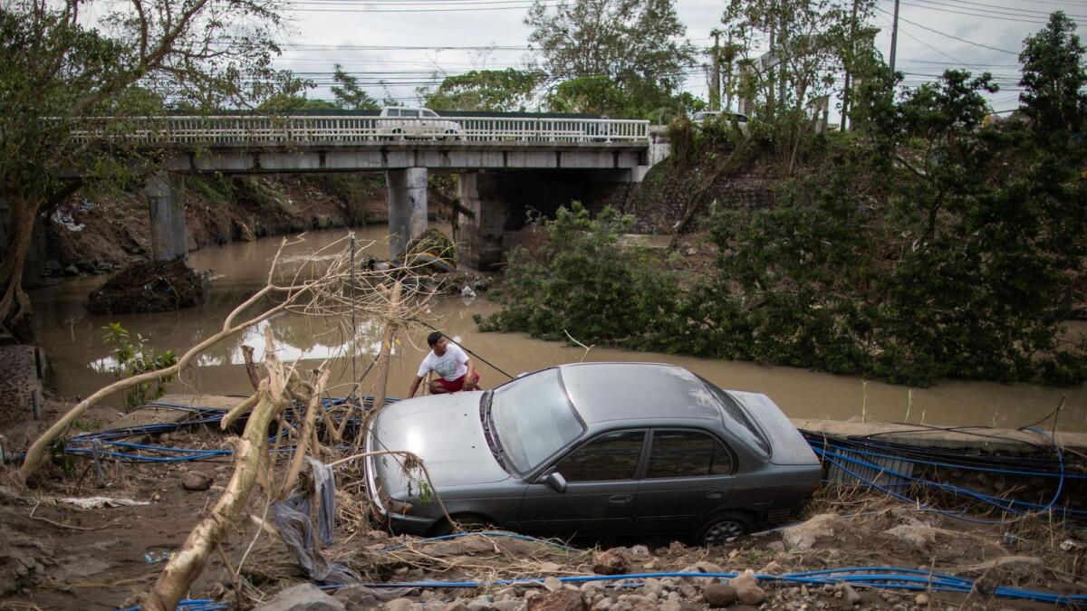 A man sits beside a car, washed away by floods caused by Typhoon Goni in Barangay San Isidro, Batangas City, Philippines, on Monday.