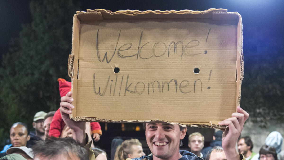 A man holds a cardboard with a 'Welcome' slogan during the arrival of refugees at the train station in Saalfeld, central Germany, Saturday, Sept. 5, 2015. (AP photo)