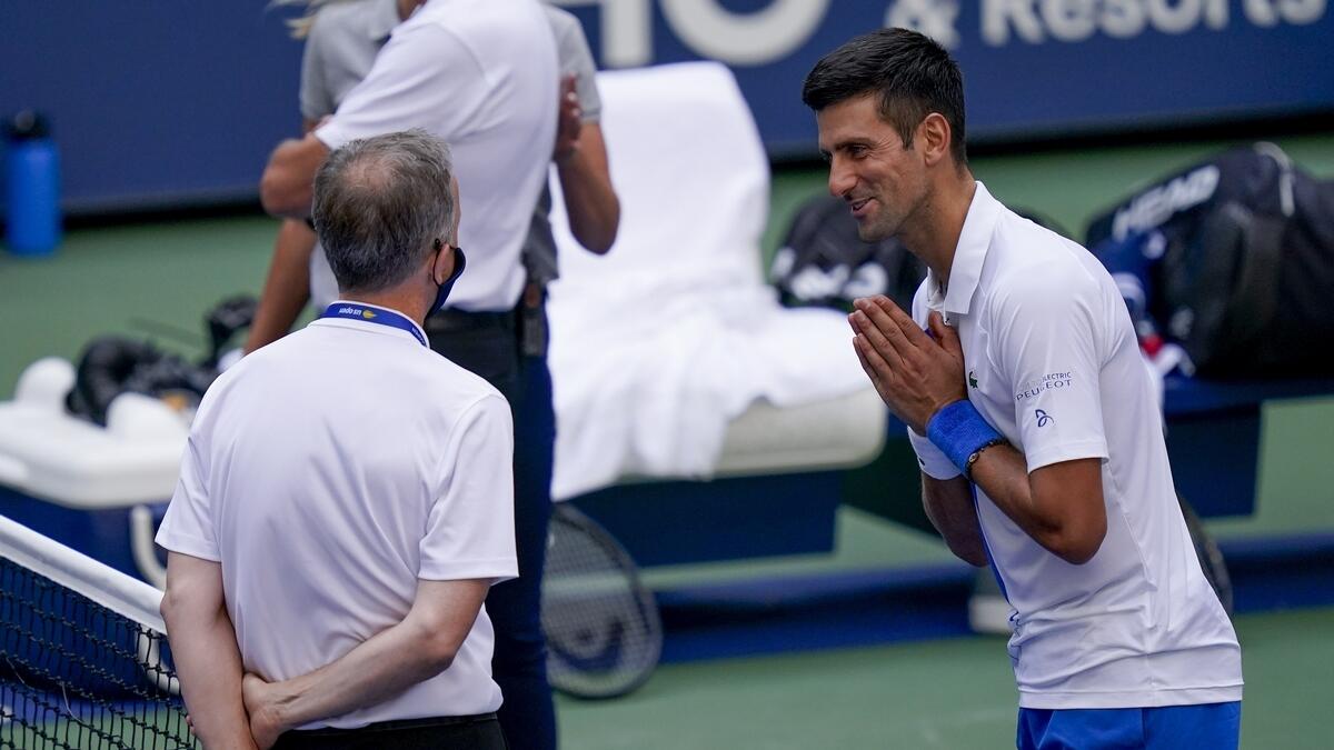 Novak Djokovic, of Serbia, talks with the umpire after inadvertently hitting a line judge with a ball after hitting it in reaction to losing a point against Pablo Carreno Busta