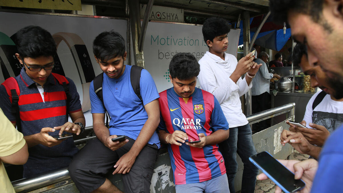 In this Sunday, July 24, 2016 photo, young Indians look at their screens at a bus station and play 'Pokemon Go' in Mumbai, India. 'Pokemon Go,' the highly addictive online game, has landed in India and thousands are out searching for pokemon characters as the mania spreads. Although it has not been launched officially in India, the augmented-reality-based game has caught on, with fans also using virtual private networks (VPNs) to change their locations and catch pokemons in New York and London while sitting in their Indian homes. (AP Photo/Rafiq Maqbool)