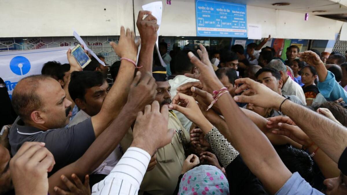 Indians stretch out their hands to collect withdrawal slips from a police officer to deposit and exchange discontinued currency notes outside the State bank of India 