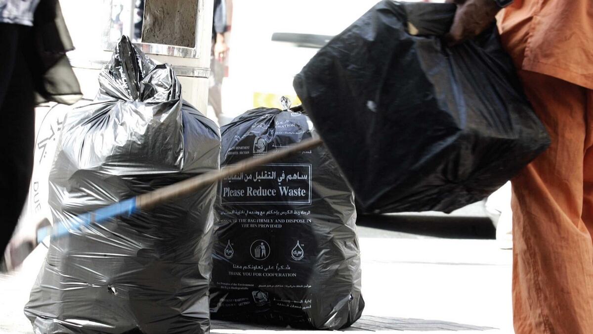 A municipality worker cleaning the street at Bur Dubai, disposing garbage bags filled with plastic bottles and tins. — File photo