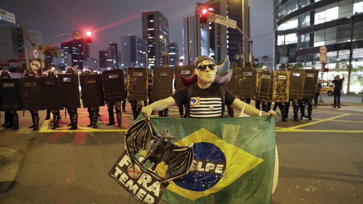 A demonstrator holds a Brazilian national flag and a sign that reads in Portuguese; 'Temer out' during a protest against President Michel Temer in Sao Paulo, Brazil, Friday, Sept. 2, 2016. Temer was sworn in as Brazil's new leader on Wednesday following the ouster of President Dilma Rousseff. (AP Photo/Andre Penner)
