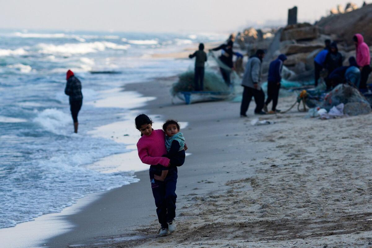 A girl walks as Palestinian fishermen work on the beach in Rafah. — Reuters