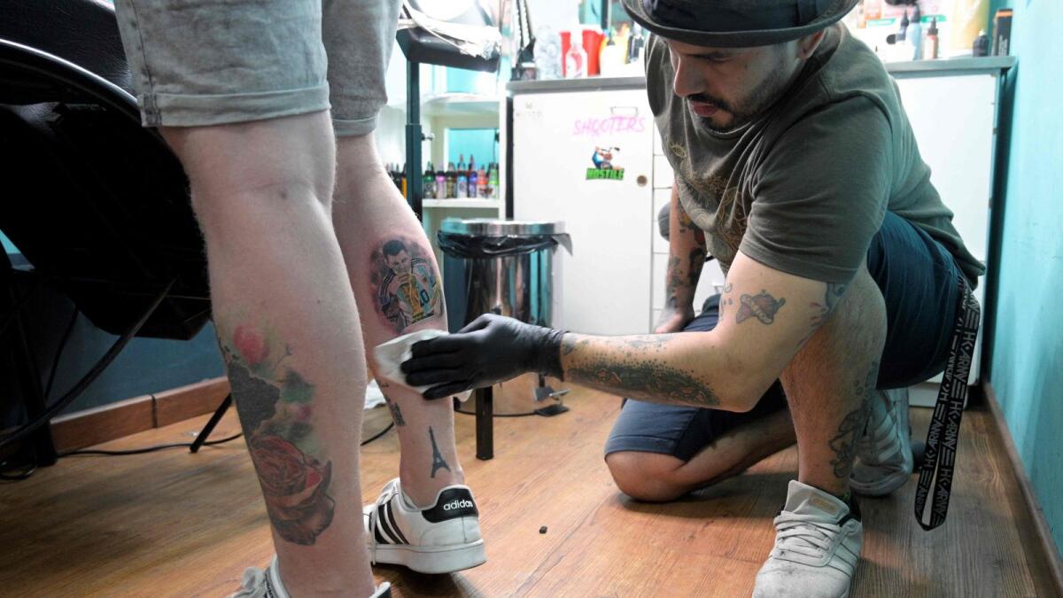 Tattooist Dario Vivas protects the tattoo of Argentina's Lionel Messi kissing the Fifa World Cup trophy on the leg of Nicolas Rechanik at Face Tattoo shop in Buenos Aires on December 23, 2022. — AFP