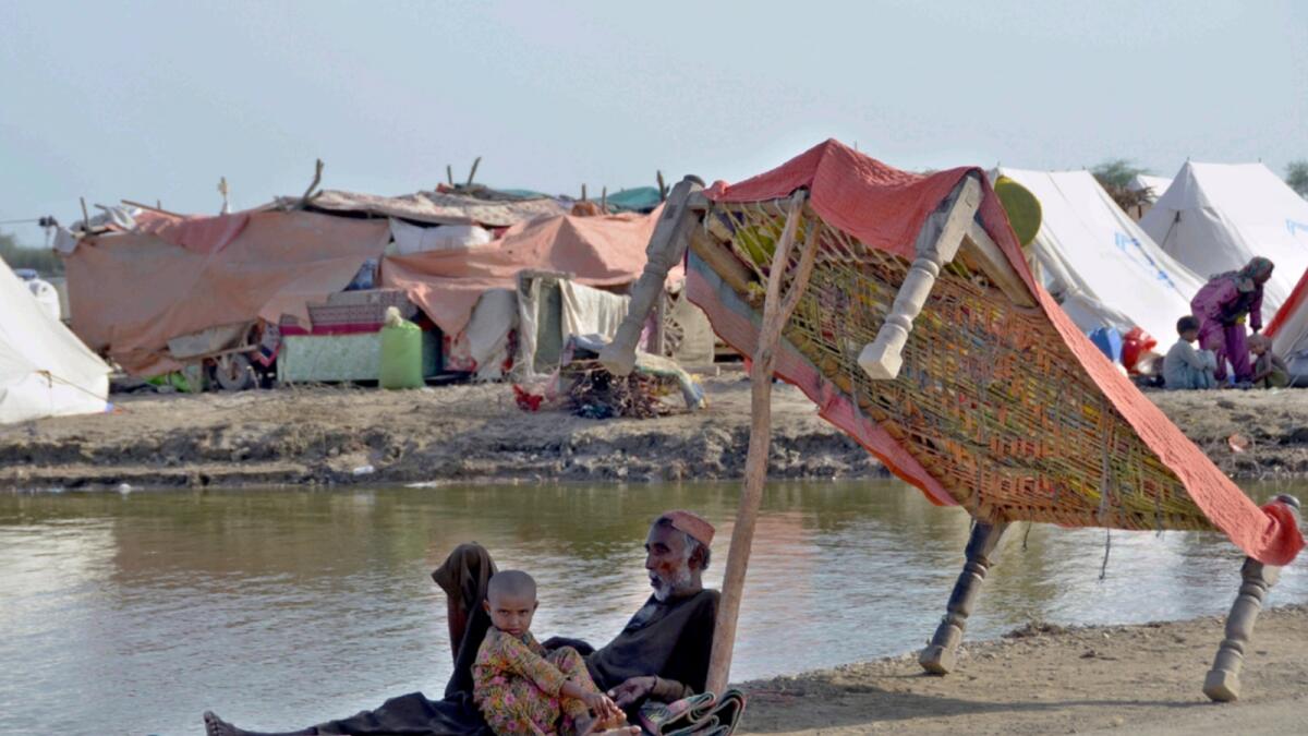 Flood victims sit under the shadow of a cot while they refuge on a roadside in Jaffarabad. — AP