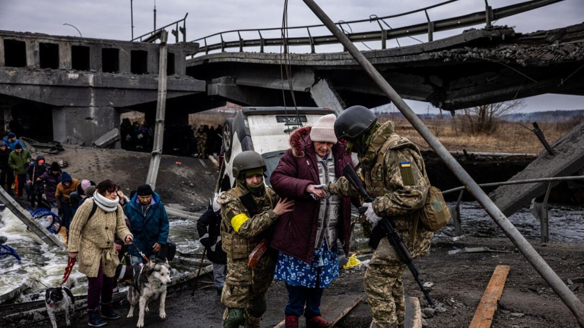 Ukrainian soldiers help an elderly woman to cross a destroyed bridge as she evacuates the city of Irpin, northwest of Kyiv, on March 7, 2022. Photo: AFP