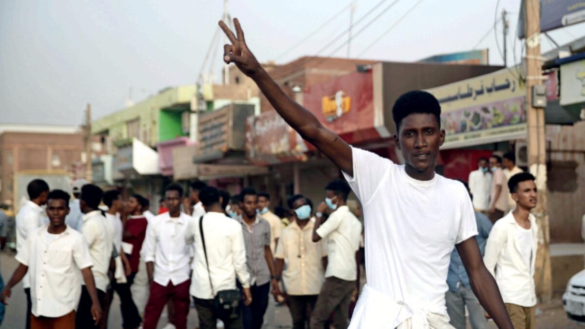 A protester flashes the victory sign, as others block a road during a protest, in Khartoum. — AP