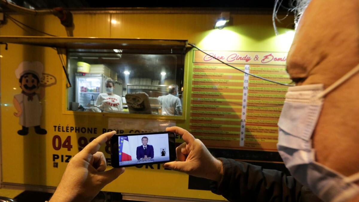 A man watches French President Emmanuel Macron on his mobile phone as he stands near a pizza van as he addresses the nation about the coronavirus disease (COVID-19) outbreak and the lockdown restrictions, in Nice, France November 24, 2020.