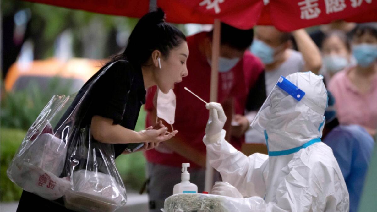 A worker wearing a protective suit swabs a woman's throat for a Covid-19 test at a coronavirus testing site in Beijing. — AP