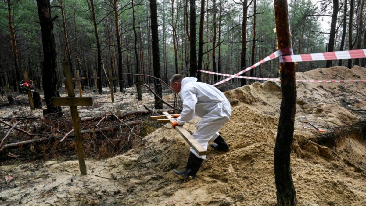 A forensic technician moves a cross in a forest on the outskirts of Izyum. — AFP
