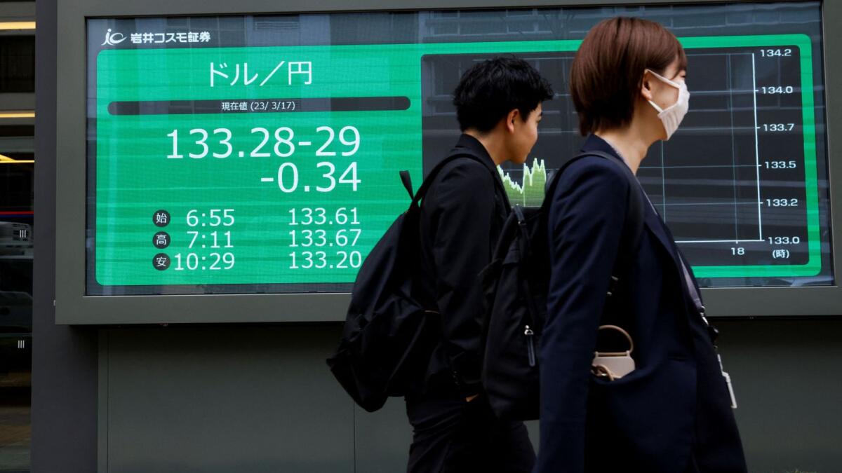 Passersby walk past an electronic board showing the exchange rate between US dollar/Japanese yen outside a brokerage, in Tokyo on Friday. - Reuters