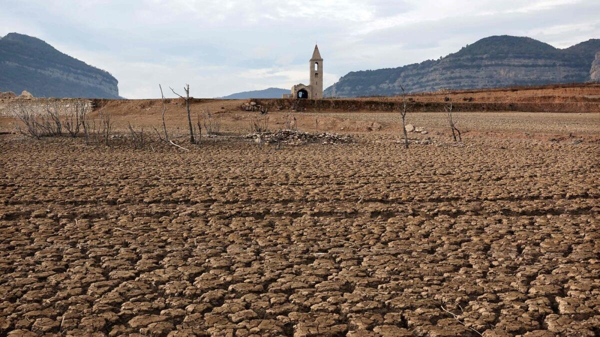 The dry soil next to the low water-level reservoir of Sau with in background Sant Roma de Sau church, in the province of Girona in Catalonia.  Catalonia struggles with historic drought for three years, with some residents already experiencing water restrictions in their daily life. — AFP