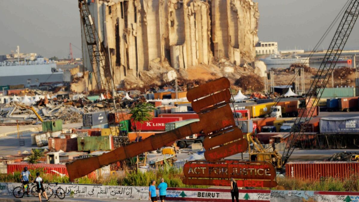 People pass next of a justice symbol monument that sits in front of towering grain silos gutted in the massive August 2020 explosion at the Beirut port that claimed the lives of more than 200 people. — AP