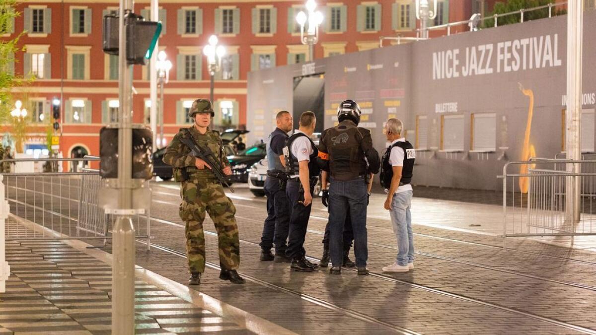 Police officers and a soldier stand by the sealed off area of an attack after a truck drove on to the sidewalk and plowed through a crowd of revelers whod gathered to watch the fireworks in the French resort city of Nice, southern France
