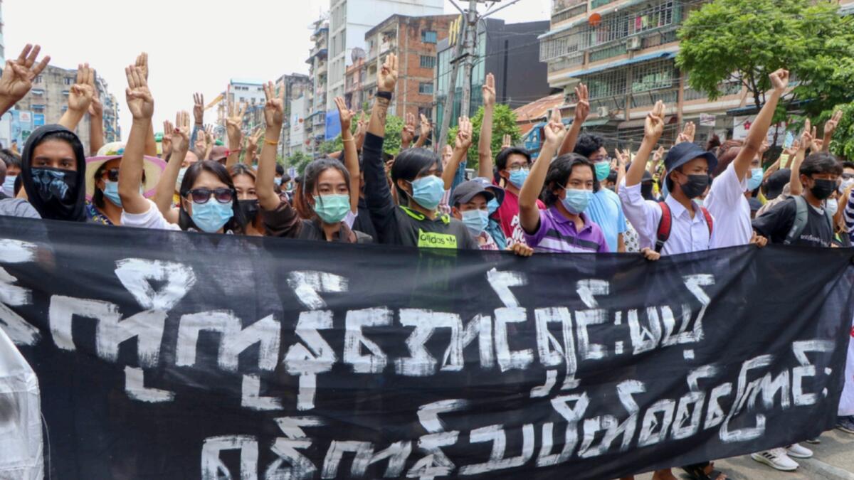 Anti-coup protesters flash the three-finger salute, holding banner read ' Yangon Strike will defeat all enemies' during a demonstration on Monday. — AP