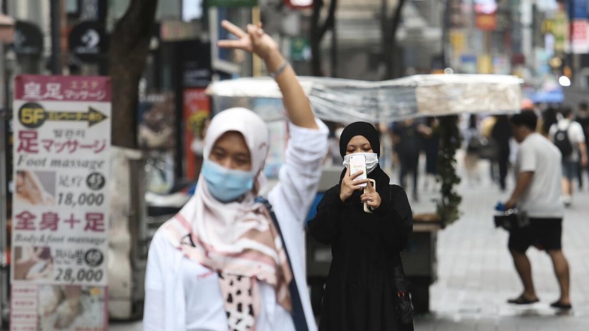 A woman wearing a face mask to help protect against the spread of the new coronavirus takes photos of her friend at a shopping street in Seoul, South Korea. Photo: AP