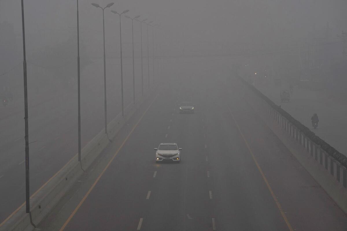 Vehicles drive with headlights on a highway as smog envelops the area and reduces visibility in Lahore on January 7, 2024.  — AP