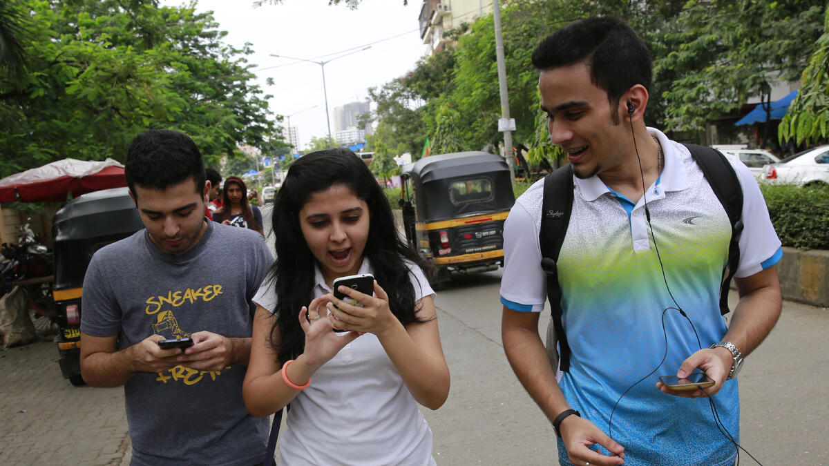 In this Sunday, July 24, 2016 photo, young Indians look at their screens as they play 'Pokemon Go' in Mumbai, India. 'Pokemon Go,' the highly addictive online game, has landed in India and thousands are out searching for pokemon characters as the mania spreads. Although it has not been launched officially in India, the augmented-reality-based game has caught on, with fans also using virtual private networks (VPNs) to change their locations and catch pokemons in New York and London while sitting in their Indian homes. (AP Photo/Rafiq Maqbool)