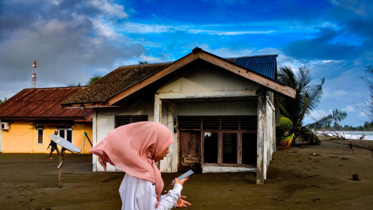 A girl walks past outside a house damaged by tidal waves at Meulaboh beach in Aceh province on July 12, 2020. Photo: AFP