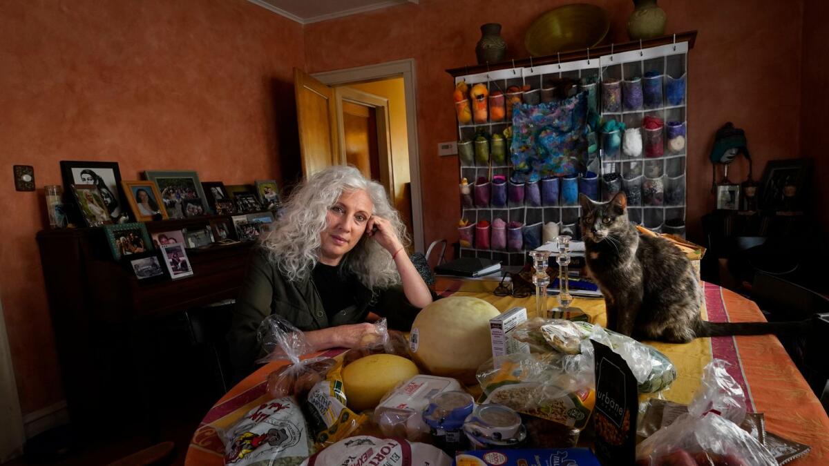 Phyllis Marder poses with her cat, Nellie, with food she recently obtained from a local food bank in the dining room of her home in Evanston, Ill., on  Nov. 5, 2020. At first, Marder, 66, did not tell anyone about going to food pantries. Then she had a change of heart. 'keeping a secret makes things get worse,' she says and 'makes me feel worse about myself, and so I decided that it was more important to talk about it.'