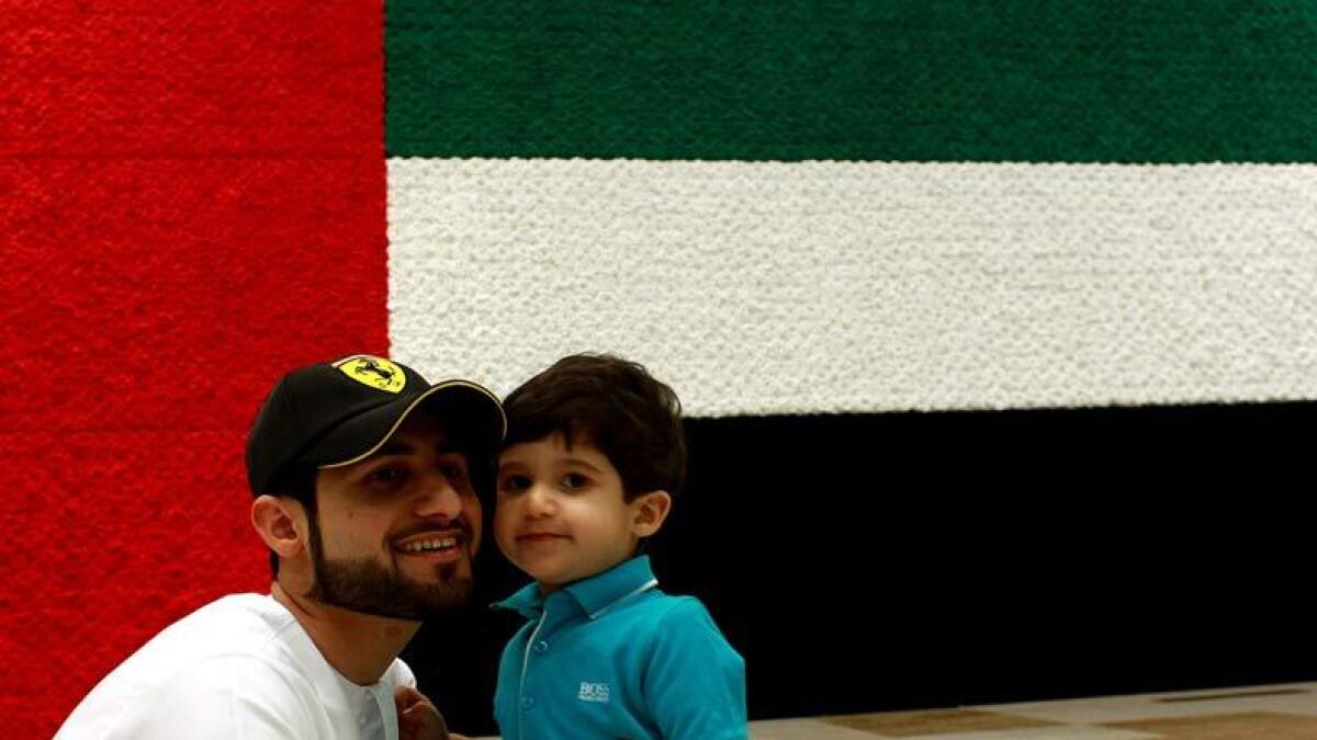Father and son posing for a photograph in front of the huge national flag displayed at Dubai International Airport. Photo by Shihab/ Khaleej Times