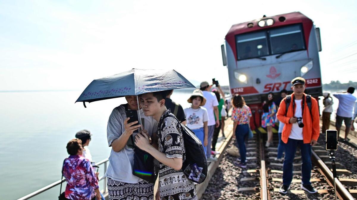 This photograph taken on November 4, 2023 shows tourists travelling aboard the popular 'Floating train' taking photographs along the railway tracks during a stop in the middle of Pasak Jolasid Dam, Thailand’s biggest reservoir in Lopburi province.— AFP
