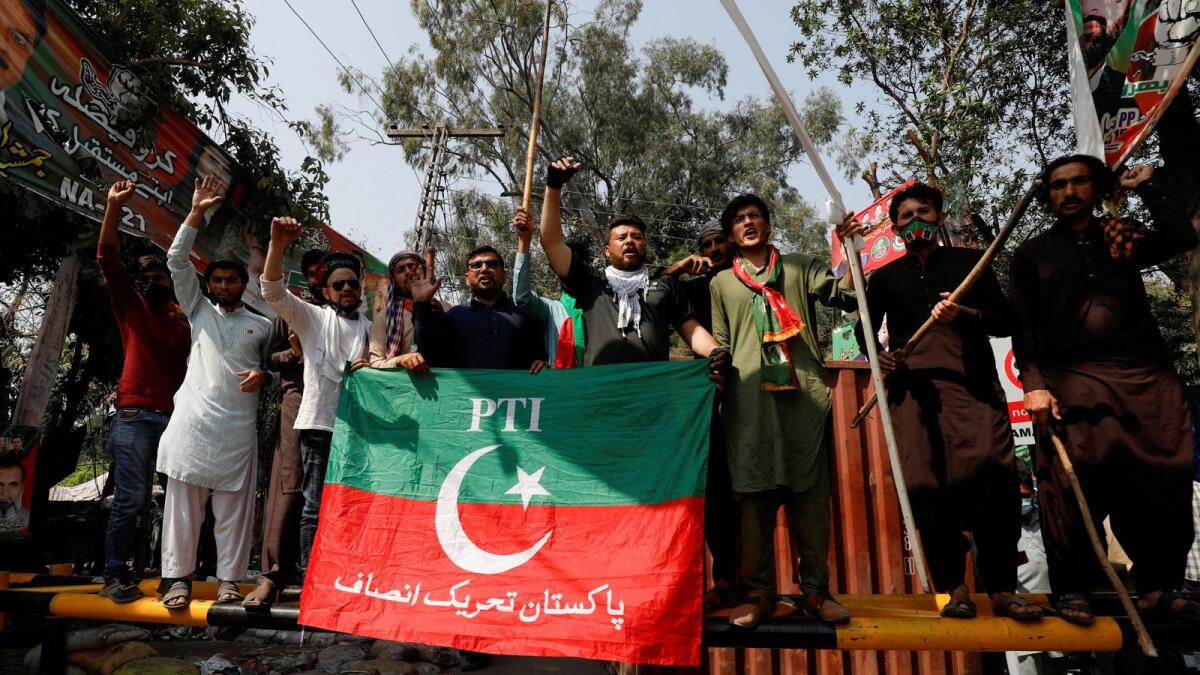 Supporters of former prime minister Imran Khan chant slogans as they stand on a barrier along a street leading to Khan's house in Lahore, Pakistan, on Thursday. — Reuters