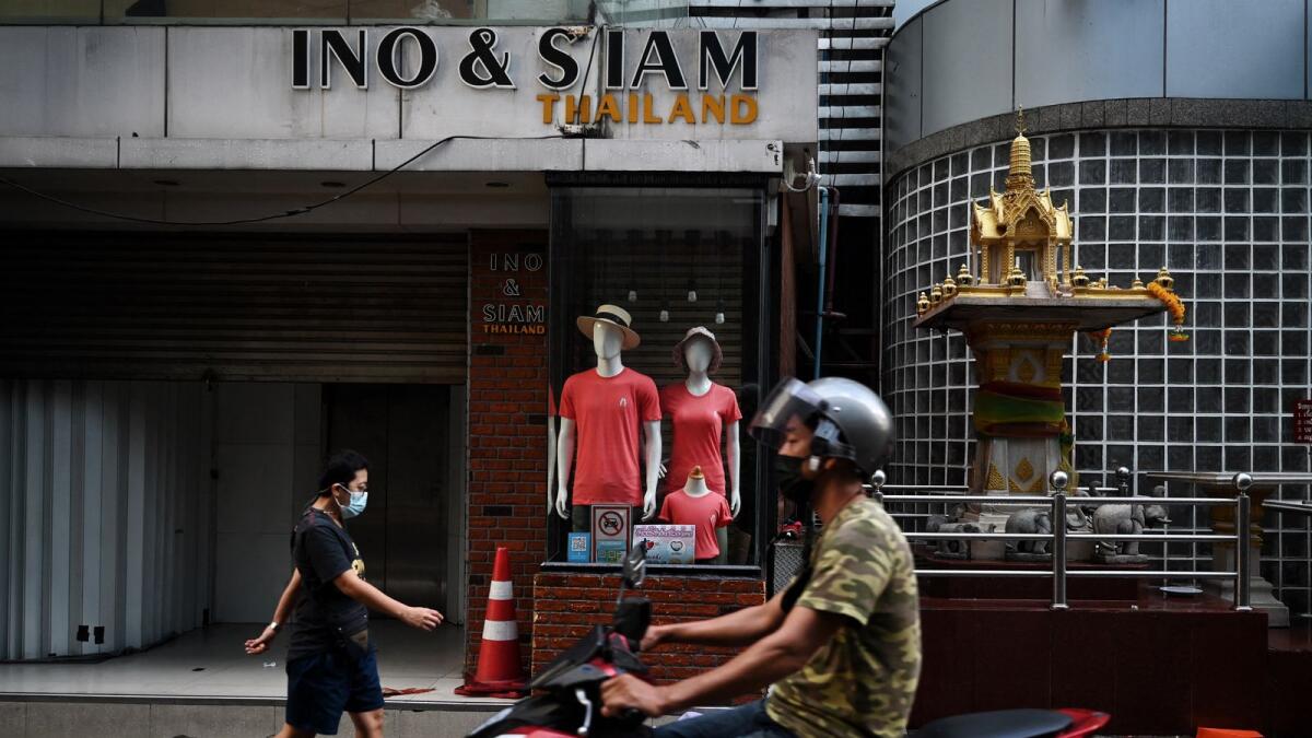 People pass by closed stores in Bangkok. Photo:  AFP