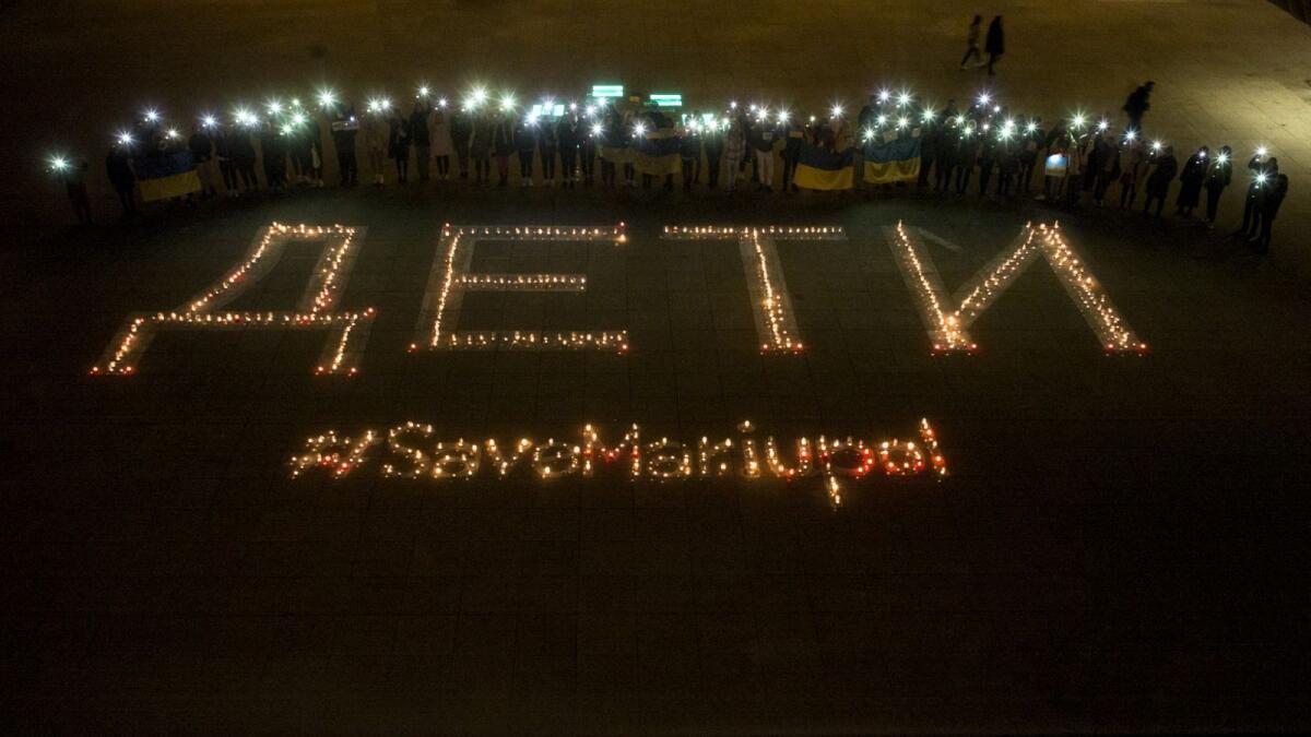 People holding flags and shining lights from their mobile phones pose next to candle lightings reading 'Children , save Mariupol' during a rally against Russia's attack on March 22, 2022 in Prague. Photo: AFP