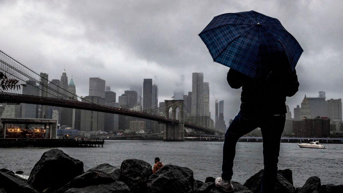 A man stands near the East River and Brooklyn Bridge with the New York skyline in the background on a Saturday, Oct. 1, 2022. -- AP