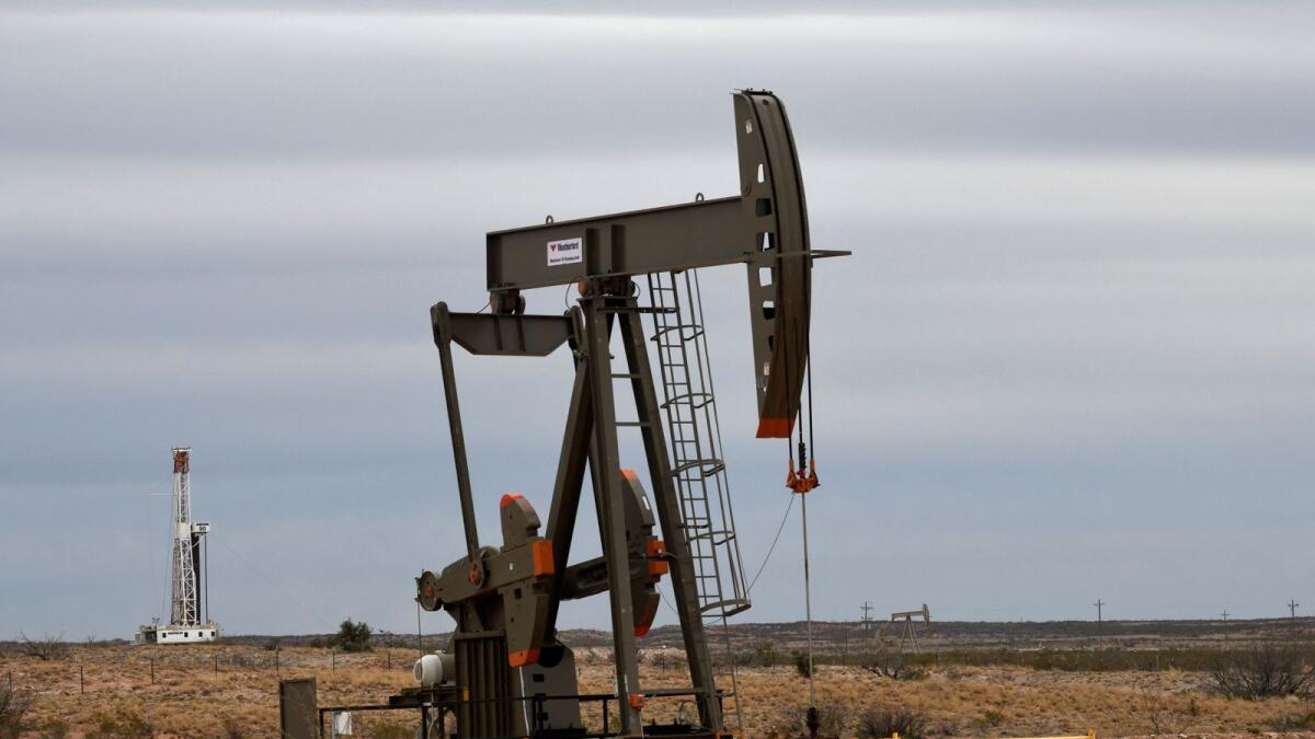 A pump jack operates in front of a drilling rig owned by Exxon near Carlsbad, New Mexico, US.