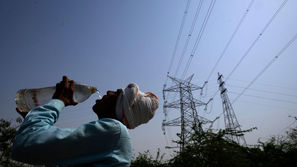 A workers quenches his thirst next to power lines in New Delhi. — AP