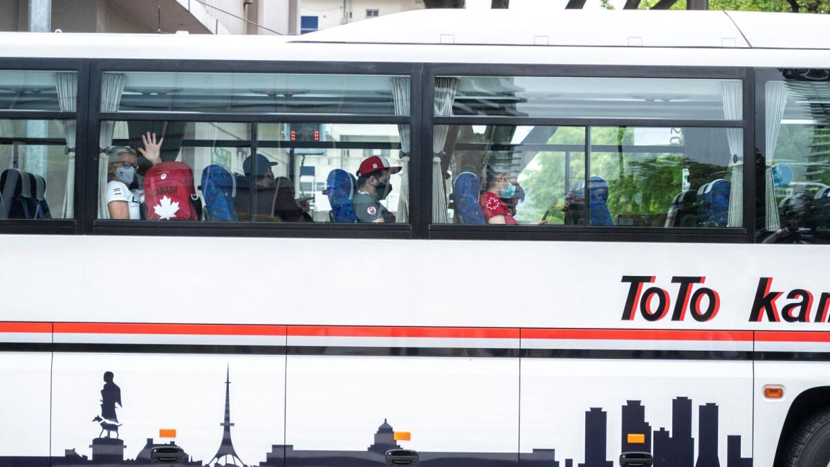 Participants from Canada wave from a bus as they arrive at the Olympic Village in Tokyo on Tuesday. (AFP)