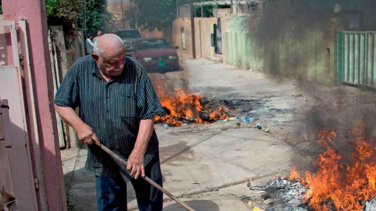 An Iraqi sweeps old pieces of furniture and garbage into a fire outside his house in Qaraqosh.