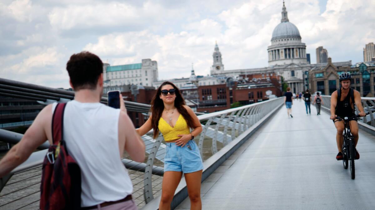 A woman poses for a photograph on the Millennium Bridge in London as temperatures are expected to again be high, hitting 31 degrees Celsius in London. Photo: AFP
