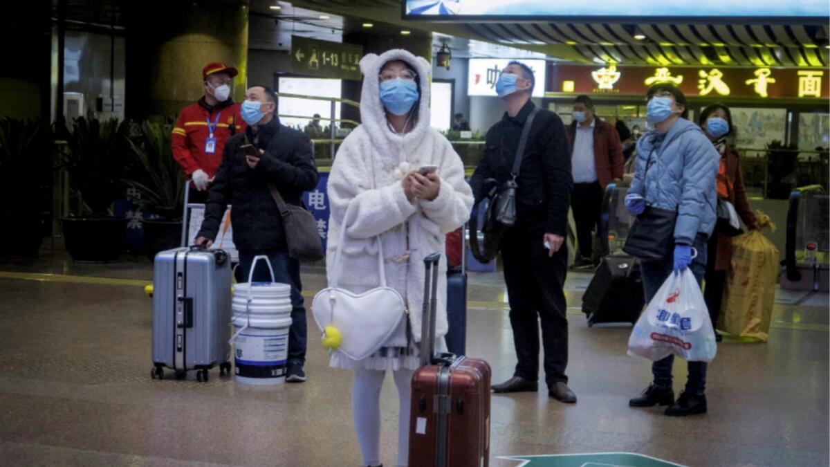 Passengers wearing protective equipment weight at a train station in Beijing. — Reuters