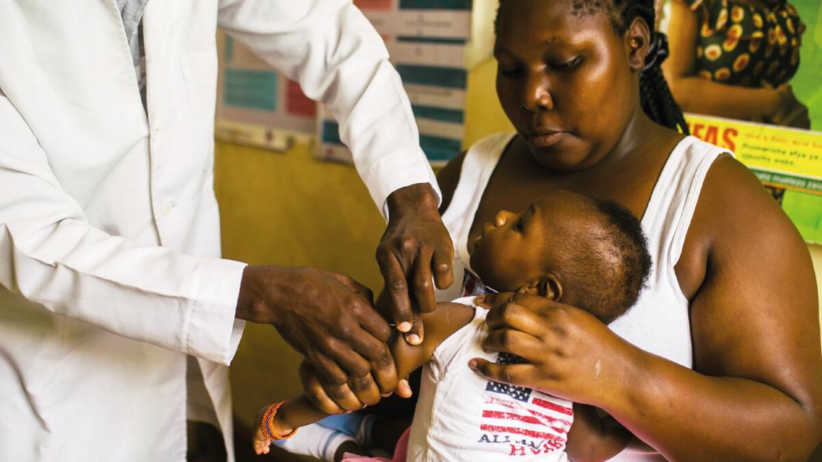 A mother holds her daughter as the girl receives a dose of malaria vaccine at the Ring Road Clinic in Nyalenda, Kenya, a poor community where the disease is endemic.  –NYT