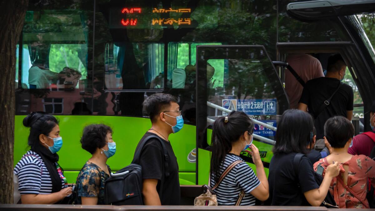 People wearing face masks to protect against coronavirus line up for a bus in Beijing. Photo: AP