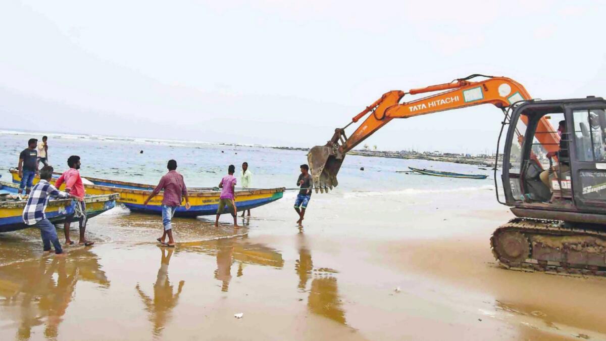 An earthmover is used to pull fishing boats ashore in view of the Cylone Jawad, in Visakhapatnam. — PTI