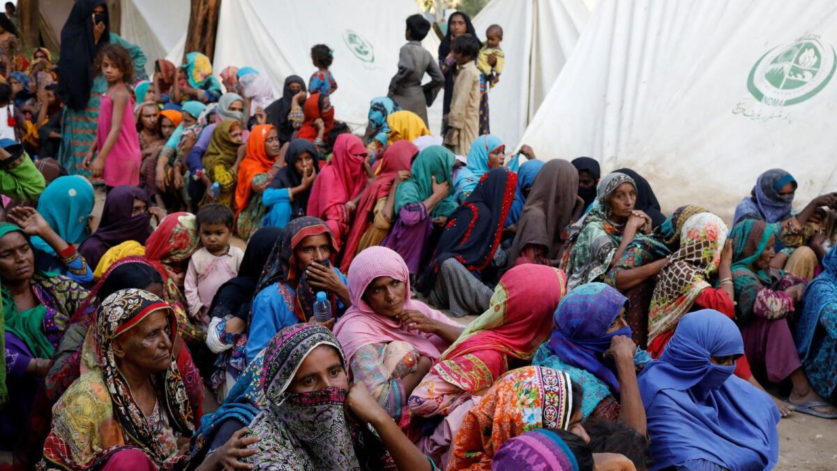 Women displaced because of the floods wait to receive food handouts while taking refuge in a camp in Sehwan, Pakistan. — Reuters