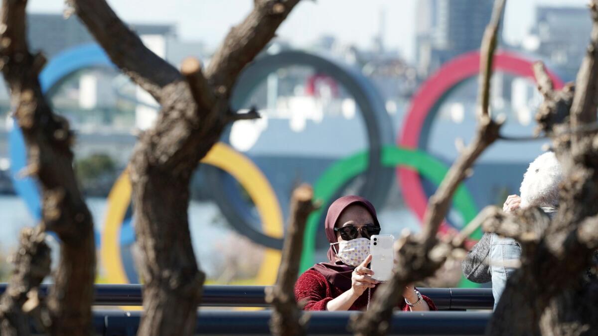 A tourist wearing a protective mask takes a photo with the Olympic rings in the background at Tokyo's Odaiba district in Tokyo. AP