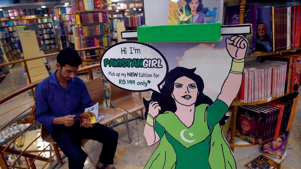 A patron reads a copy of the Pakistan Girl comic series at a book store in Islamabad next to an image of the main character Sarah. — AFP