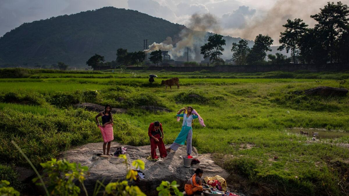 Smoke rises from a coal-powered steel plant in the background as village girls get ready after taking a bath in a stream at Hehal village near Ranchi, India. — AP