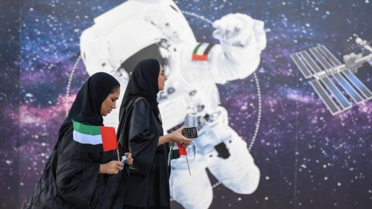 Women walk past an illustration depicting an astronaut with the Emirati national flag outside Mohammed Bin Rashid Space Centre (MBRSC) in Dubai. — AFP file photo