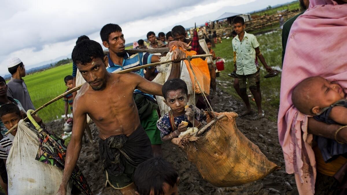 A Rohingya carries a child in a sack and walks through rice fields after crossing over to the Bangladesh side of the border.-AP