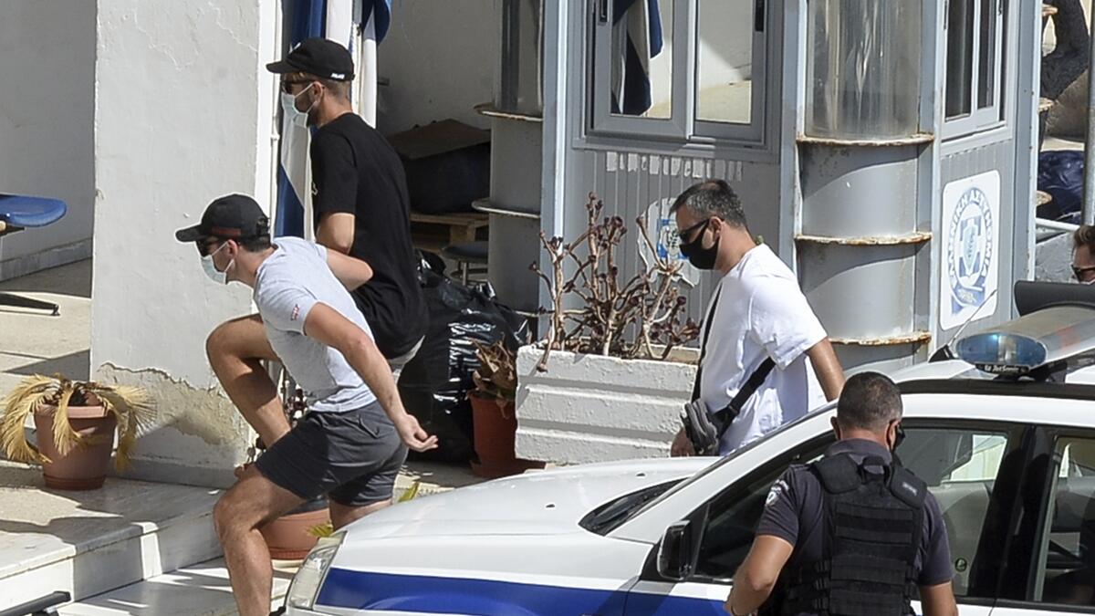 Harry Maguire, left, is escorted by plain clothed police officers as he arrives at the police station on the Aegean island of Syros, Greece