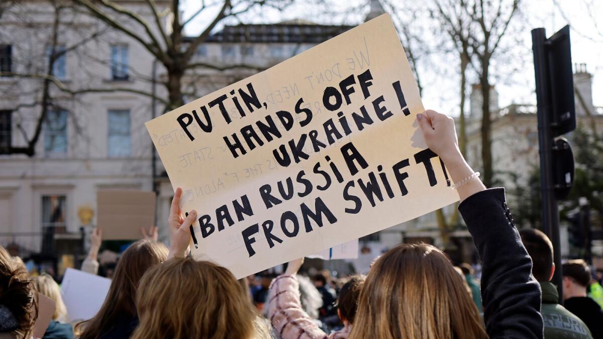 Demonstrators hold a placard calling on Russia to be banned from the Swift banking system as they attend a protest rally outside of the Russian Embassy in London - AFP
