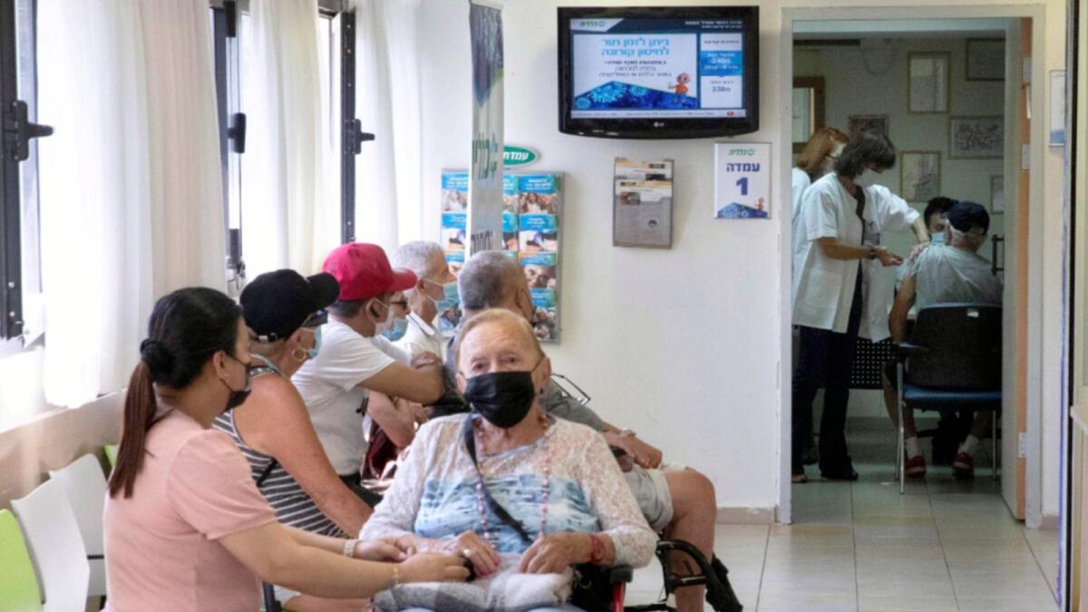 Israelis wait in line as a man receives a booster dose of Pfizer Covid-19 vaccine in Tel Aviv. — AP file