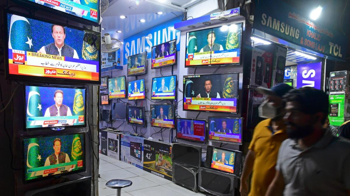 Pedestrians listen to Pakistan's Prime Minister Imran Khan addressing the nation on television at a market in Karachi on March 31, 2022. Photo: AFP